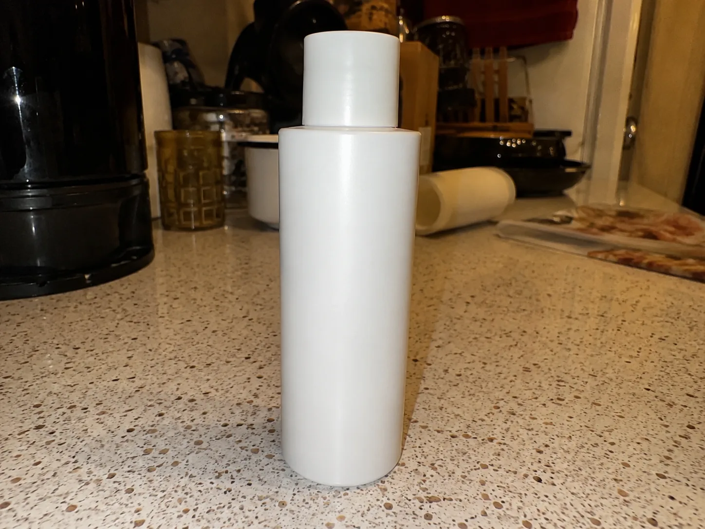Phone snapshot of a skincare bottle on a cluttered kitchen counter